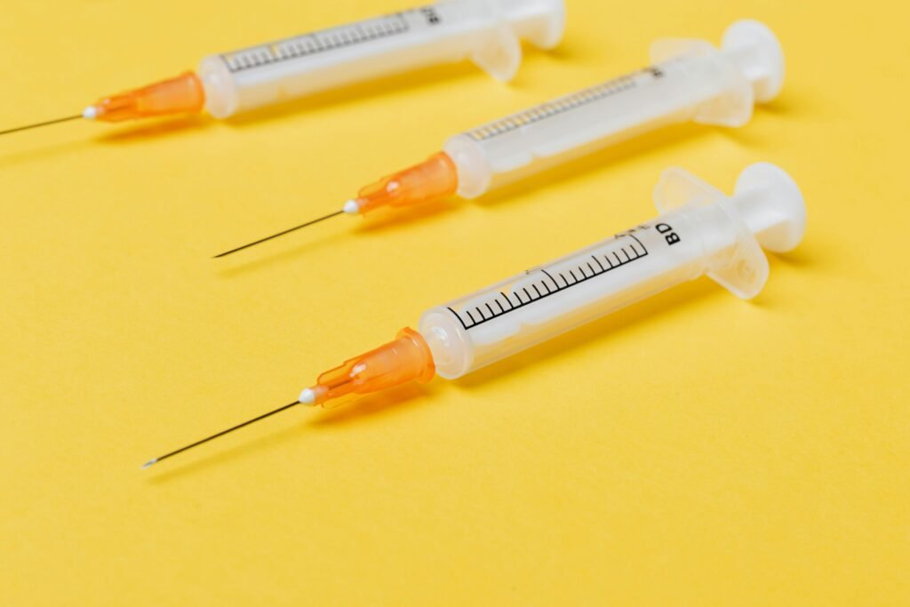 Close-up of three syringes on a vibrant yellow background, emphasizing health tools.